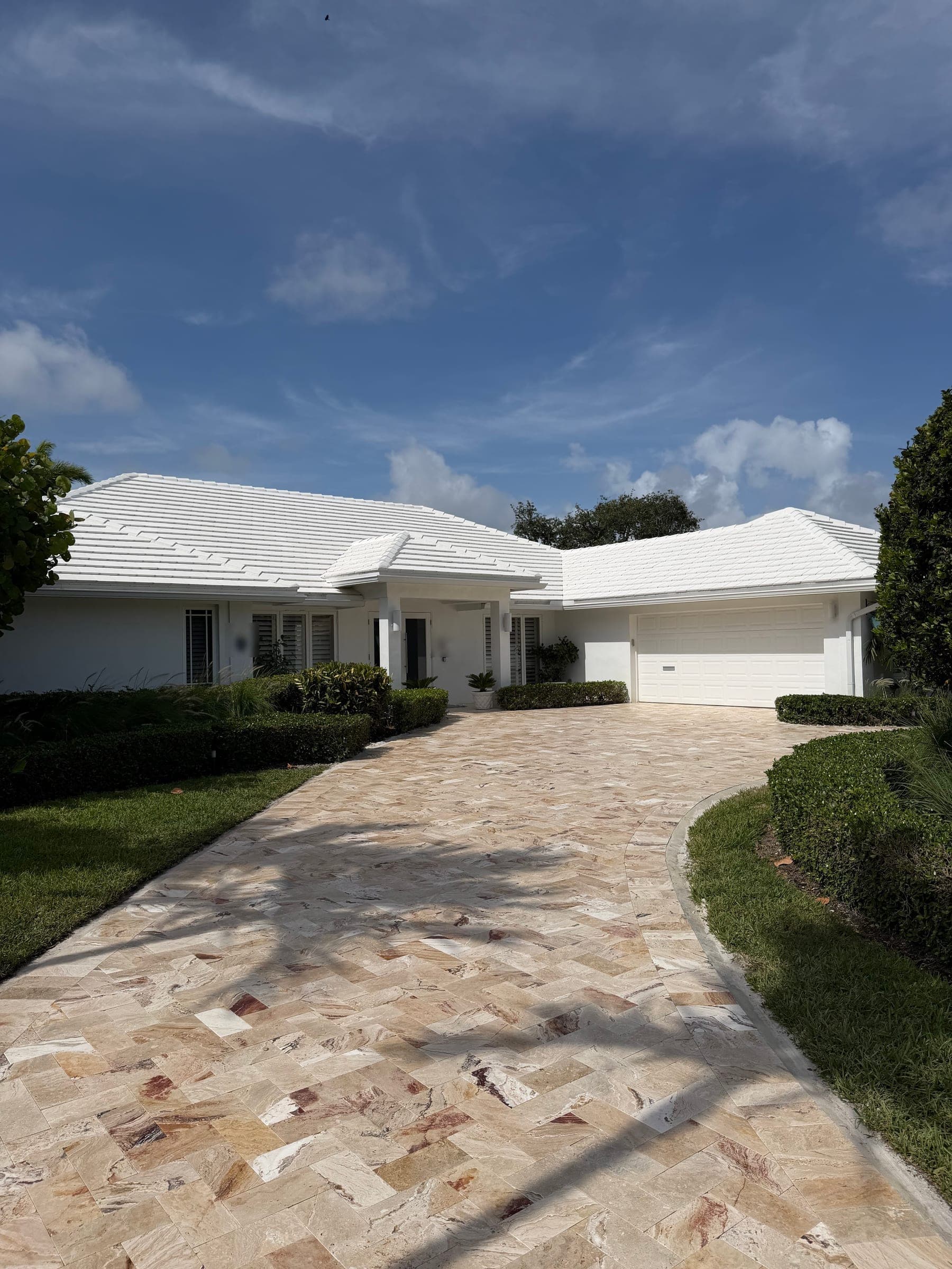 Completed travertine paver driveway leading to a white single-story home with a two-car garage