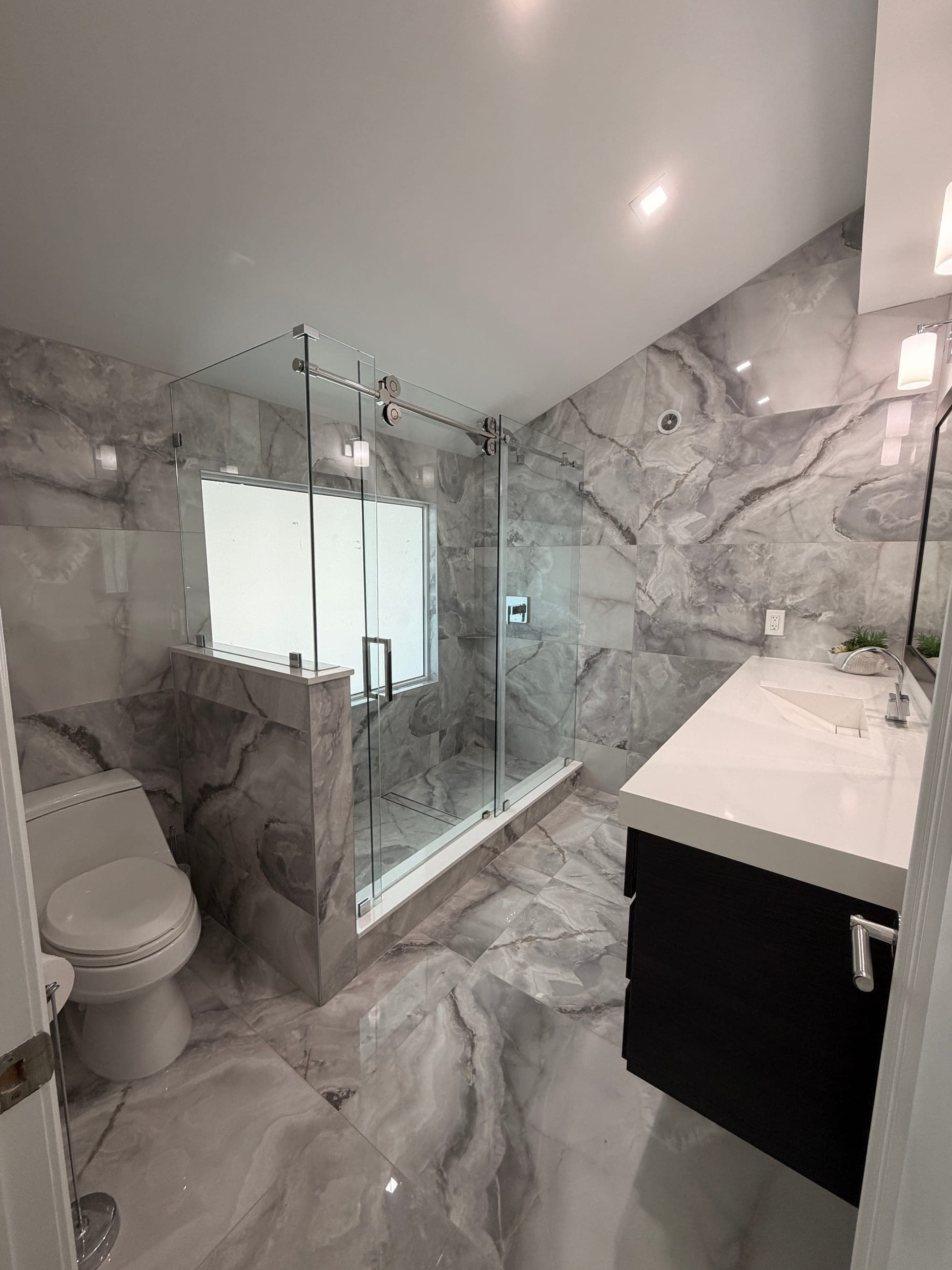 Completed modern bathroom remodel with frameless glass shower, marble-look tile, and updated vanity