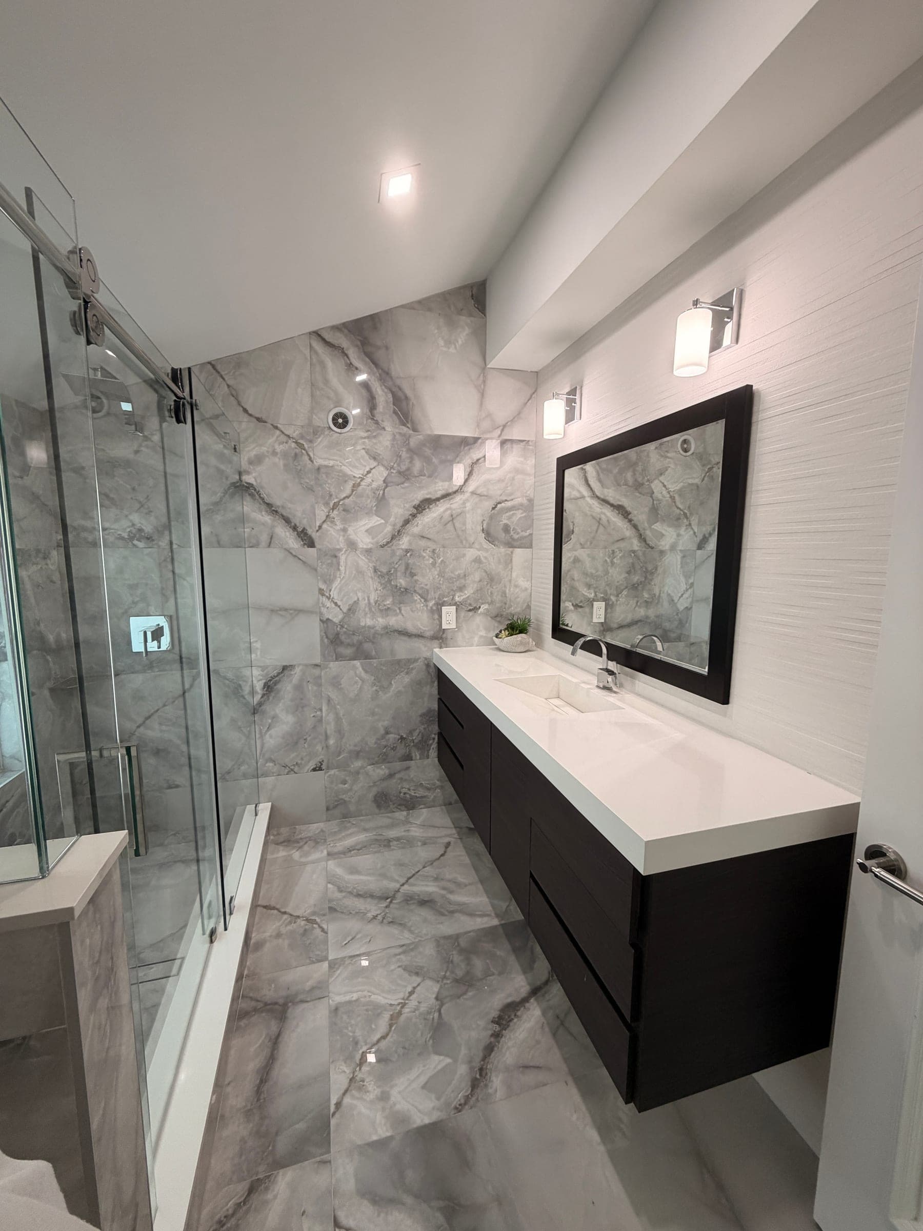 Marble-look tiled shower with frameless glass enclosure and sliding door hardware