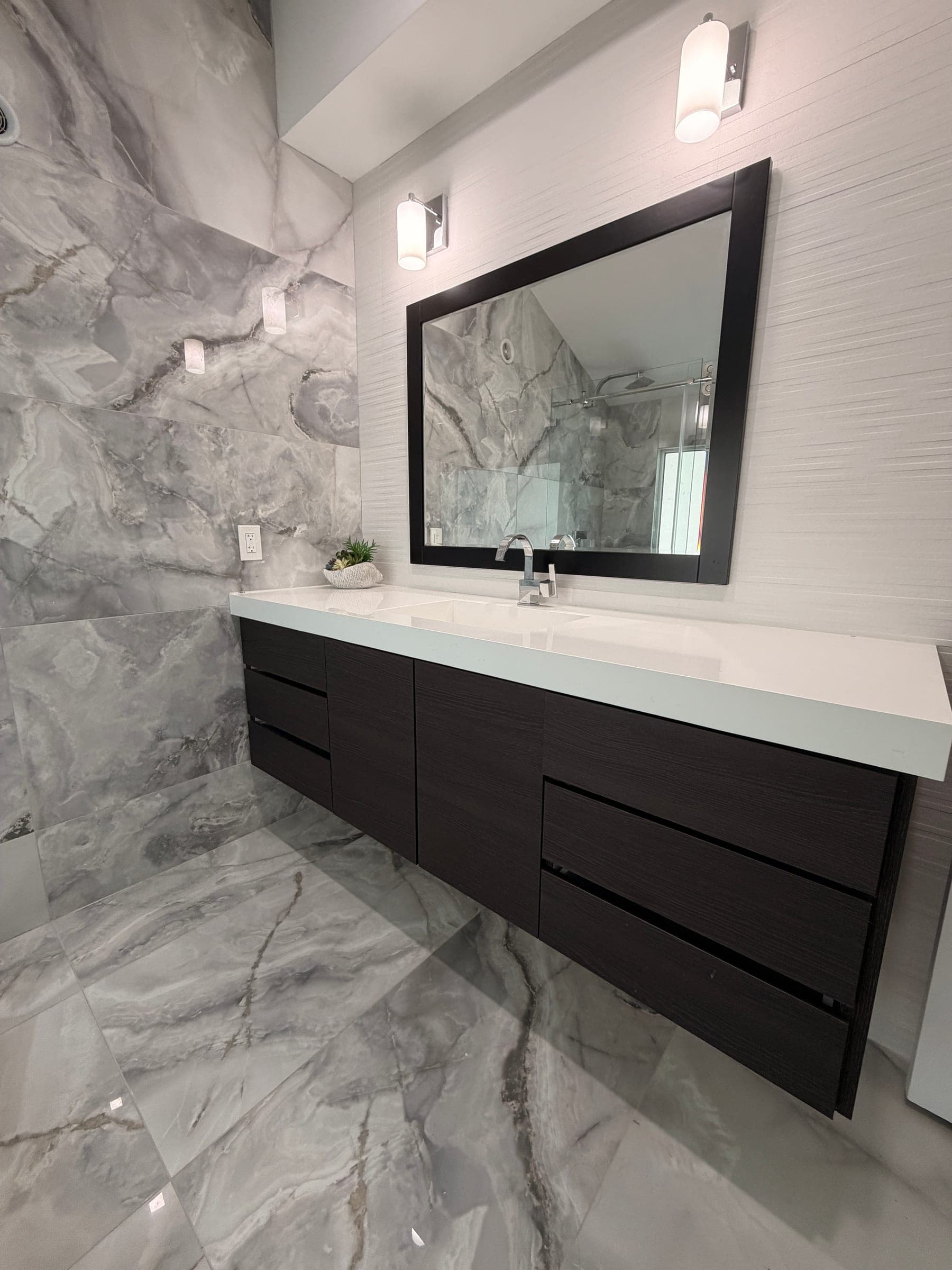 Toilet and glass shower enclosure with marble-look tile in remodeled bathroom