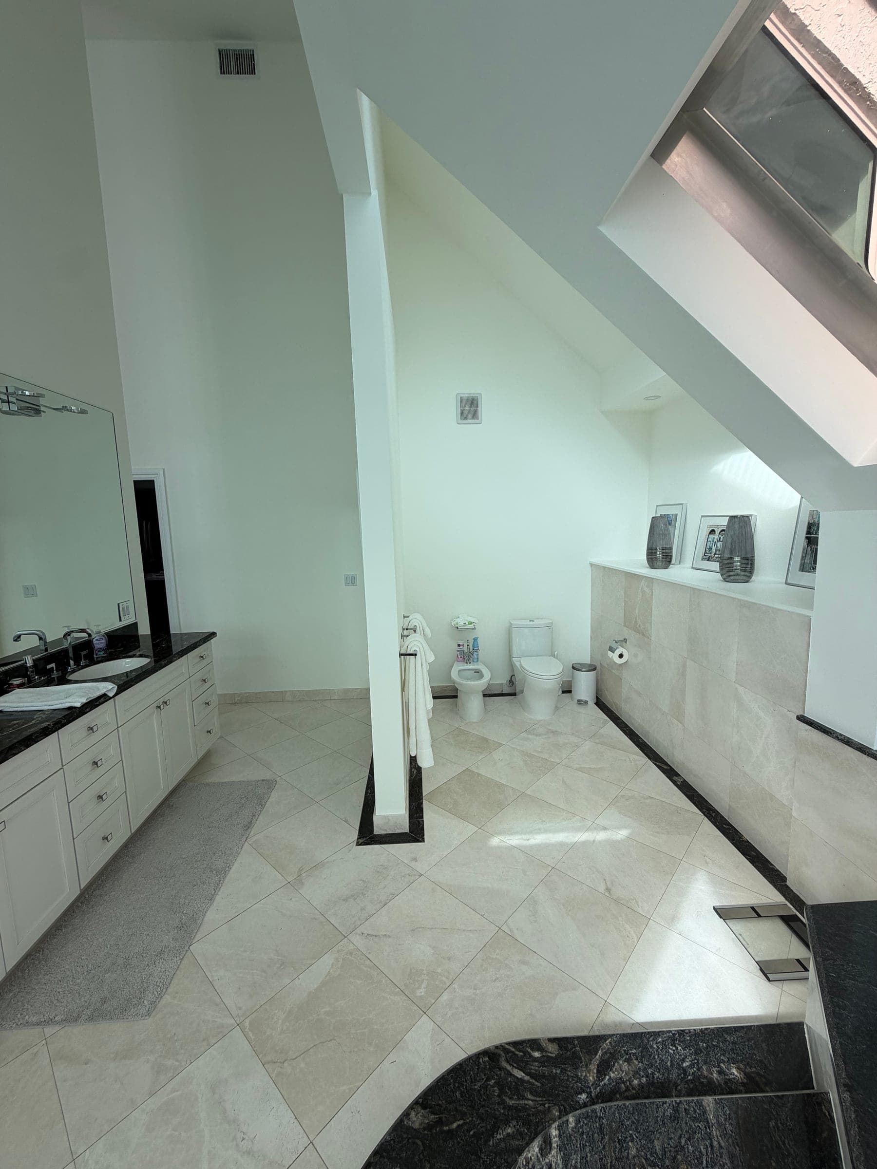 Primary bathroom vanity, toilet area, and marble tile with black granite tub in the background