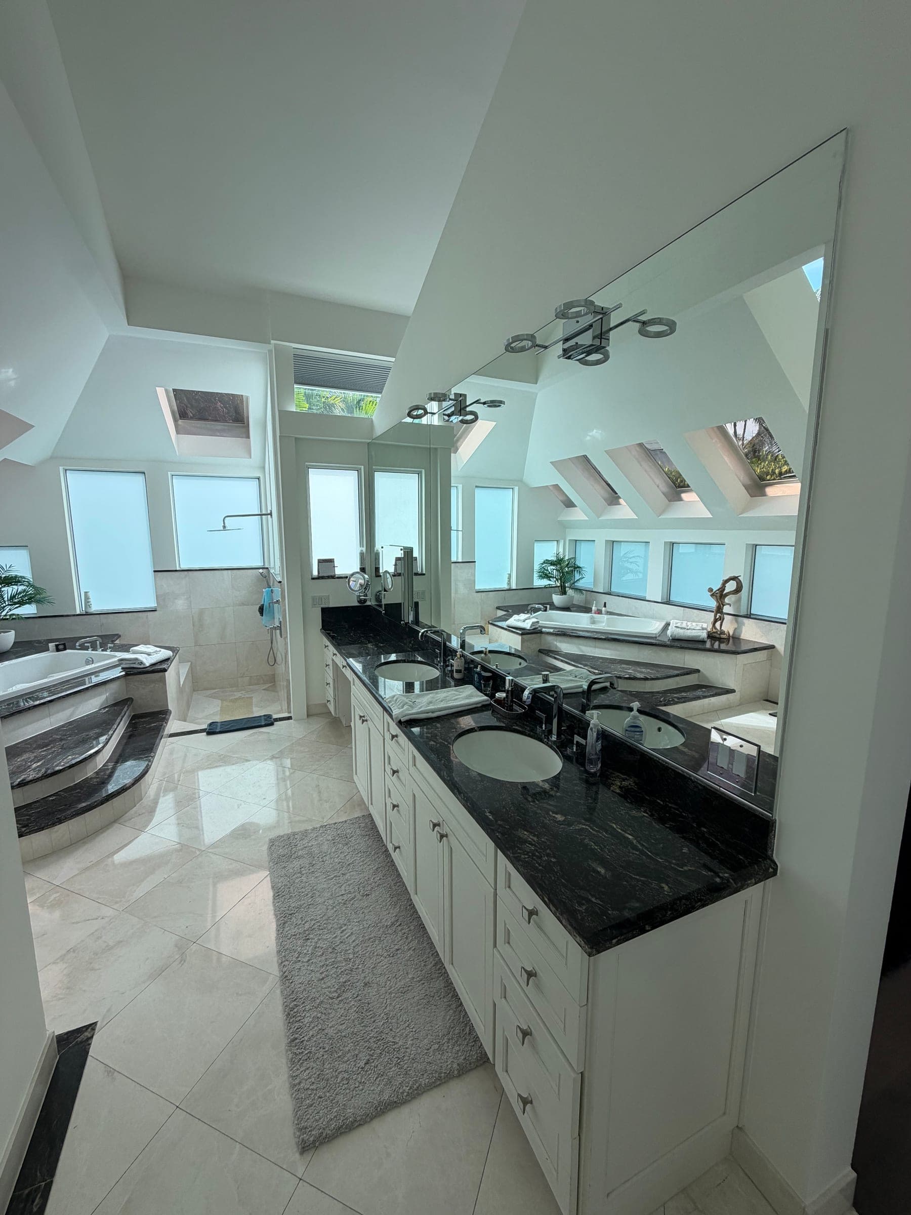 Primary bathroom double vanity with black granite countertop, reflecting the sunken tub and skylights