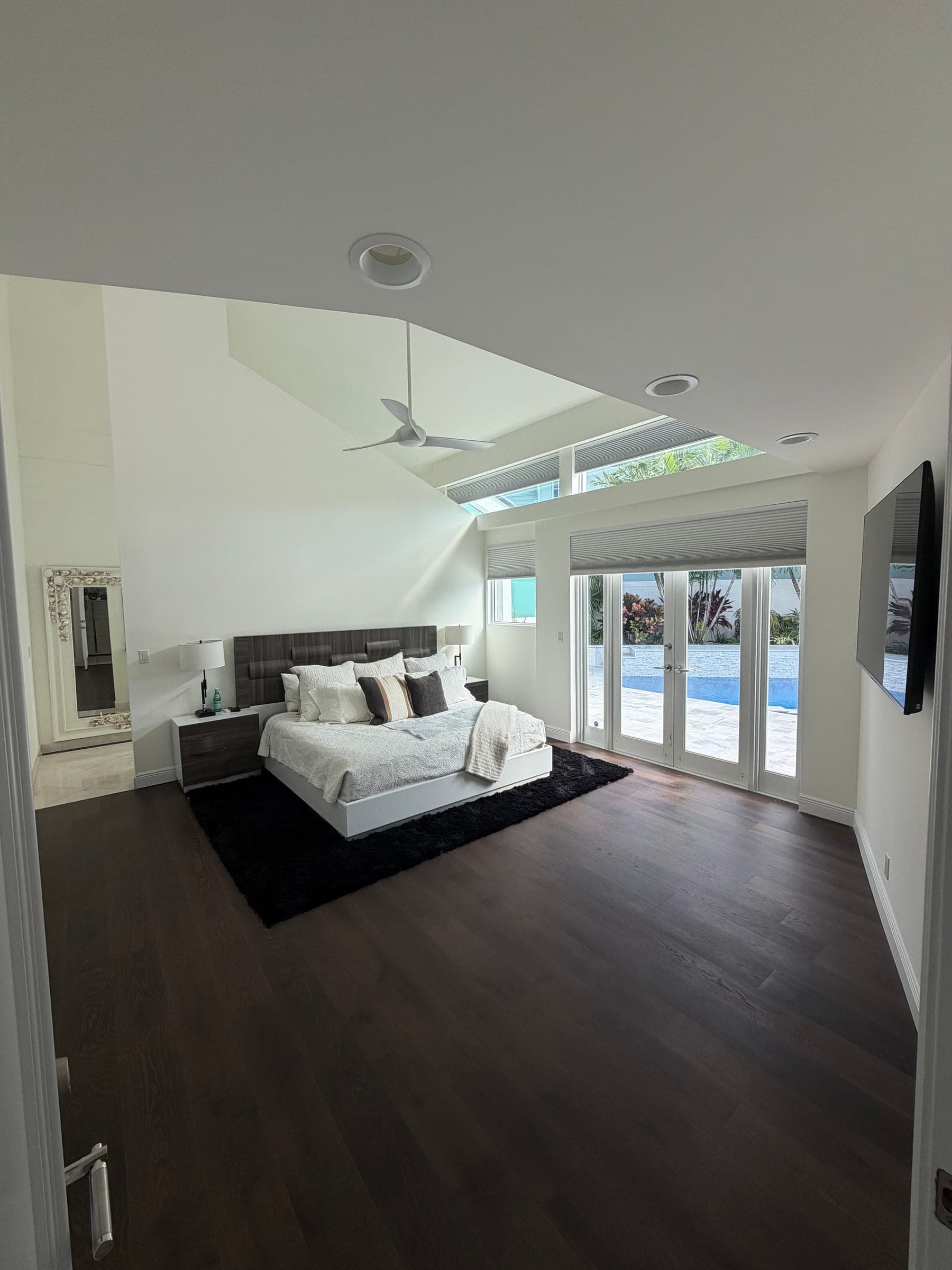 Renovated primary bedroom with upholstered bed, dark wood flooring, and French doors to the pool patio