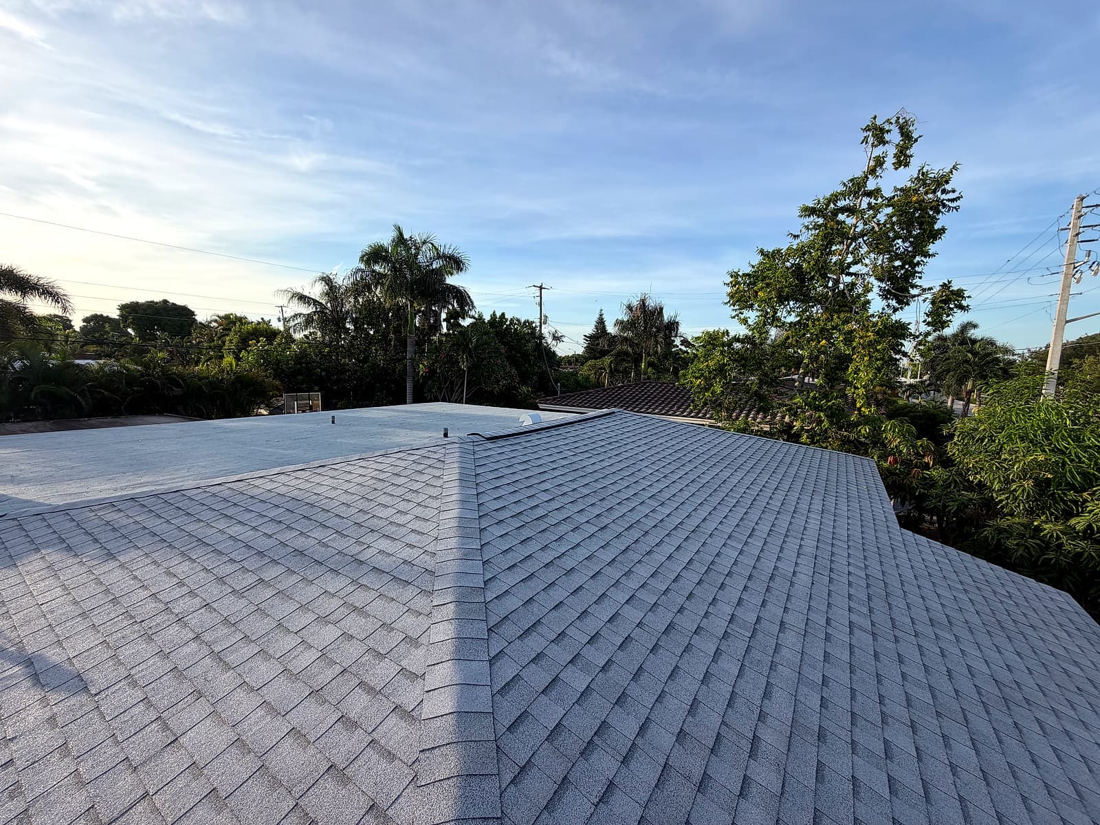 Completed architectural shingle roof alongside the finished modified bitumen flat roof section